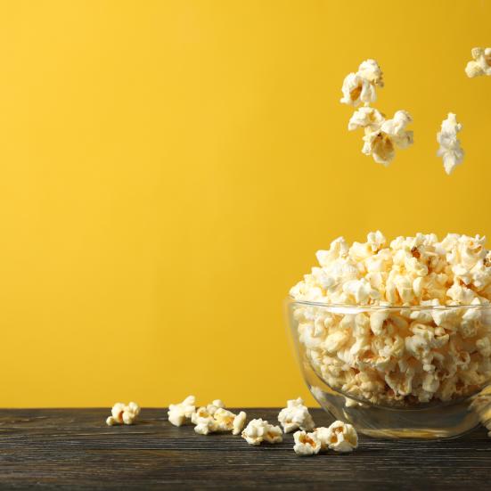 Billedet forestiller en glasskål fyldt med popcorn. Væggen er i en stærk gul farve, der giver et godt blikfang.