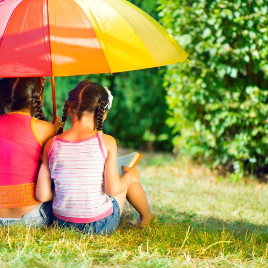 Billedet forestiller to børn der sidder med ryggen til. De er begge piger. Den ene har en bog i hænderne, mens den anden holder en paraply med "regnbuefarver" over dem.