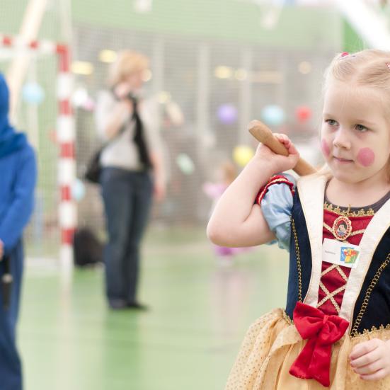 Billedet forestiller en pige til fastelavnsfest. Hun er klædt ud om en prinsesse og holder køllen klar til at slå katten af tønden.