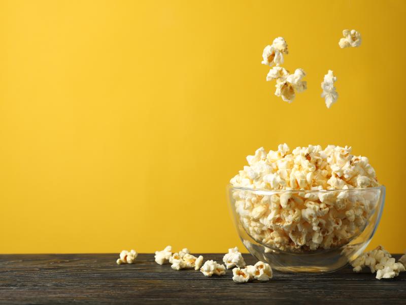 Billedet forestiller en glasskål fyldt med popcorn. Væggen er i en stærk gul farve, der giver et godt blikfang.