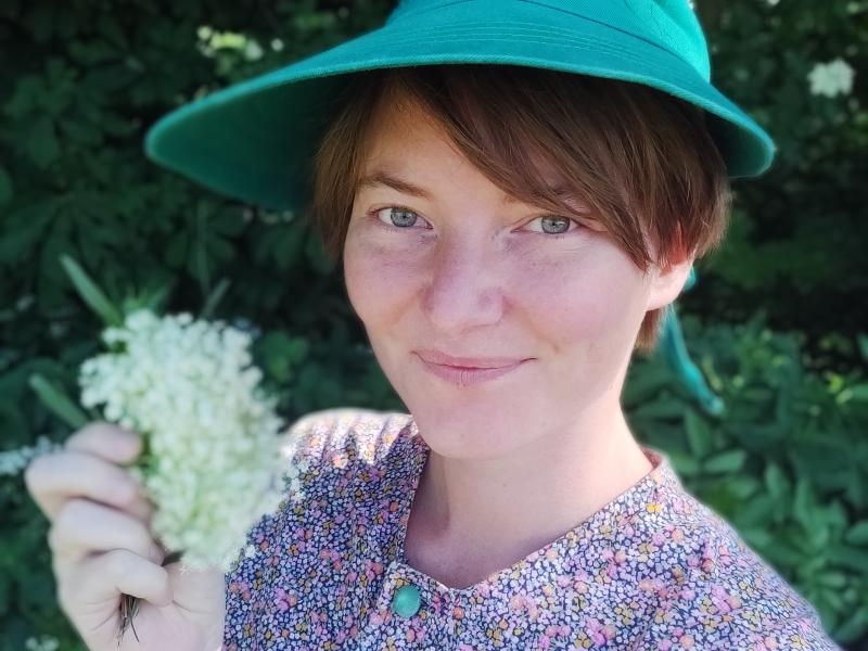 Billedet forestiller en smilende kvinde med en hyldeblomst i hånden