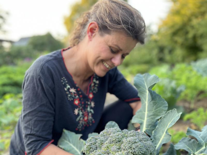 Billedet forestiller en smilende kvinde, der høster en broccoli